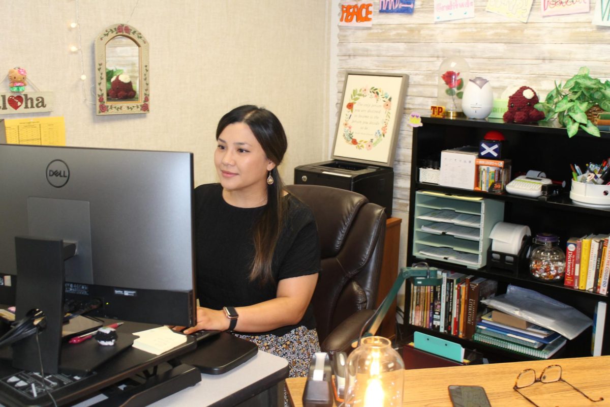 Fraline Vargas, ELD and freshman English teacher, works on the computer before class. Books, pens and decorations fill the shelf behind her. 