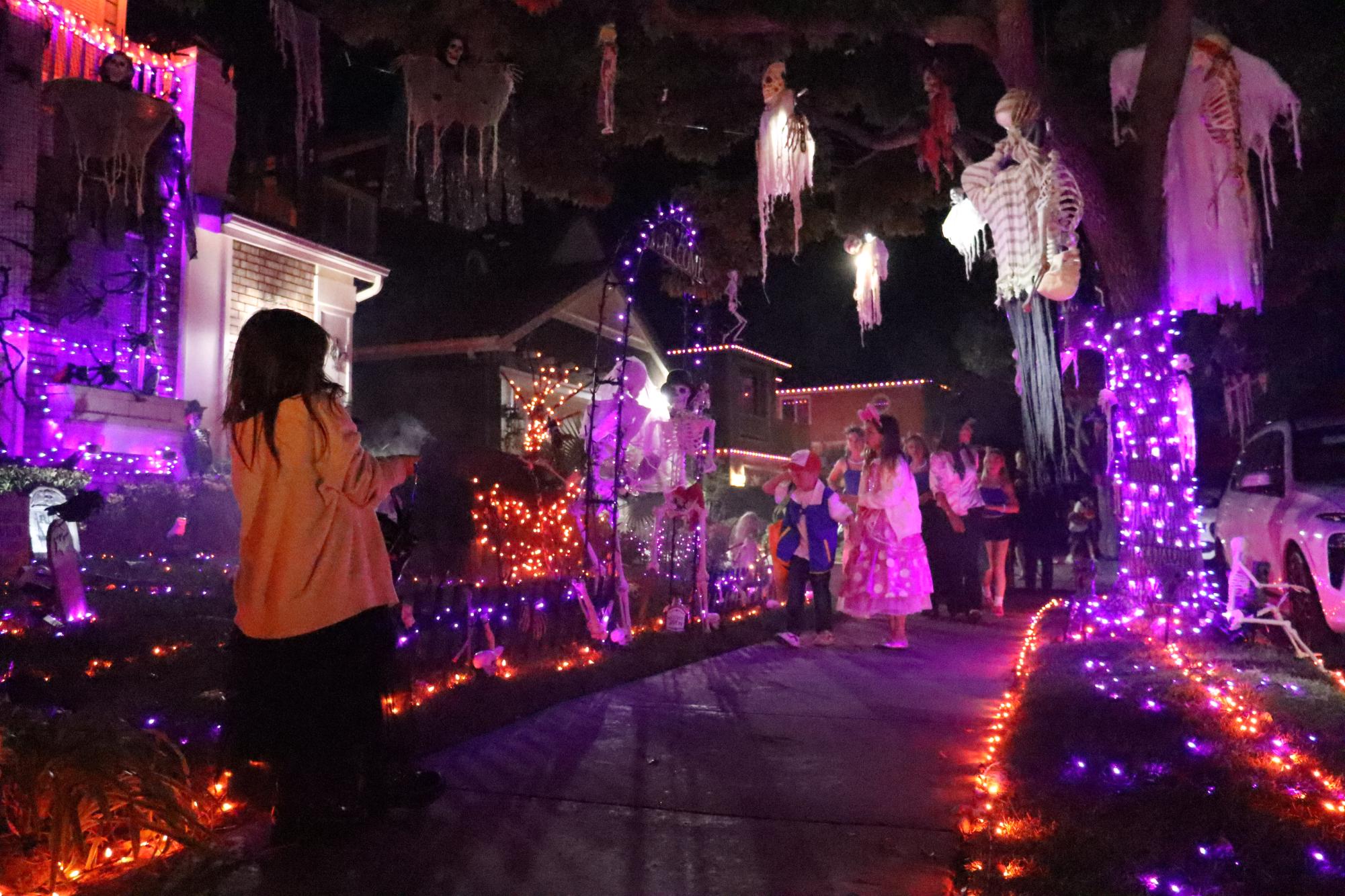 Trick-or-treaters stand in awe before a married skeleton couple and small ghosts. This house was one of many on the street that take pride in their vibrant Halloween decorations.