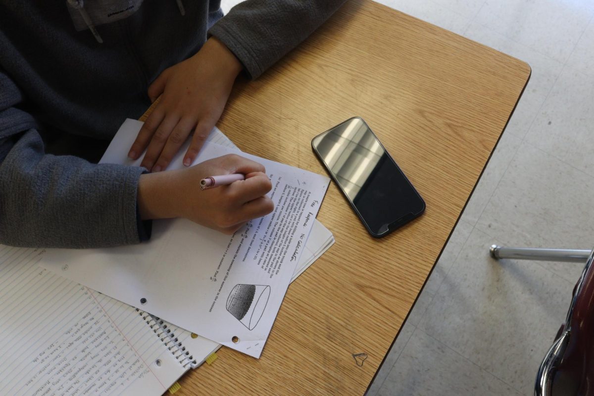 A student works on schoolwork in the presence of their phone. Governor Newsom signed the Phone-Free Schools Act on Sept. 23, which requires all California school districts to create and adopt a policy that limits or prohibits smartphone use.