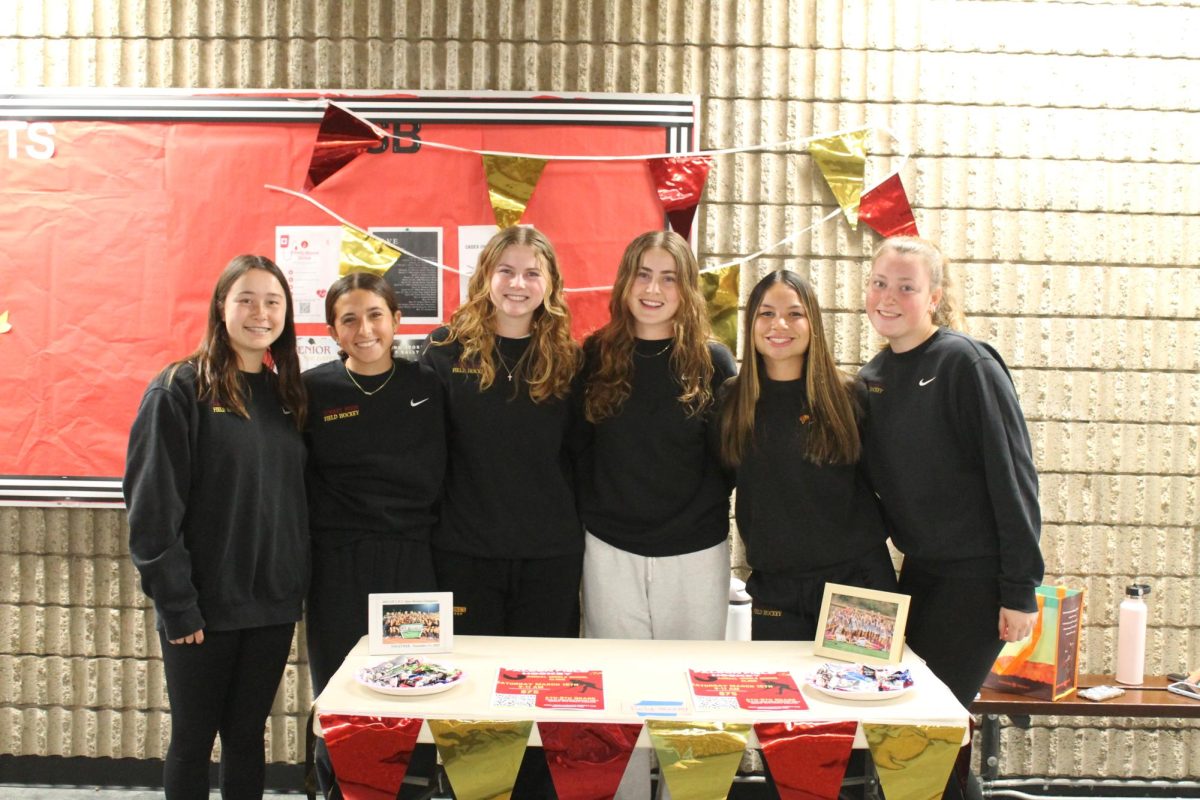 Their station colored with cardinal and gold, the field hockey team gathers for a picture. Freshman Welcome Night included booths by various sports, such as football and gymnastics. Left to right: Izzy Adams (9), Dylan Rietti (10),  Morgan Christie (11), Sophie Herman (10), Ava Hauer (10) and Kara Dunlop (11).