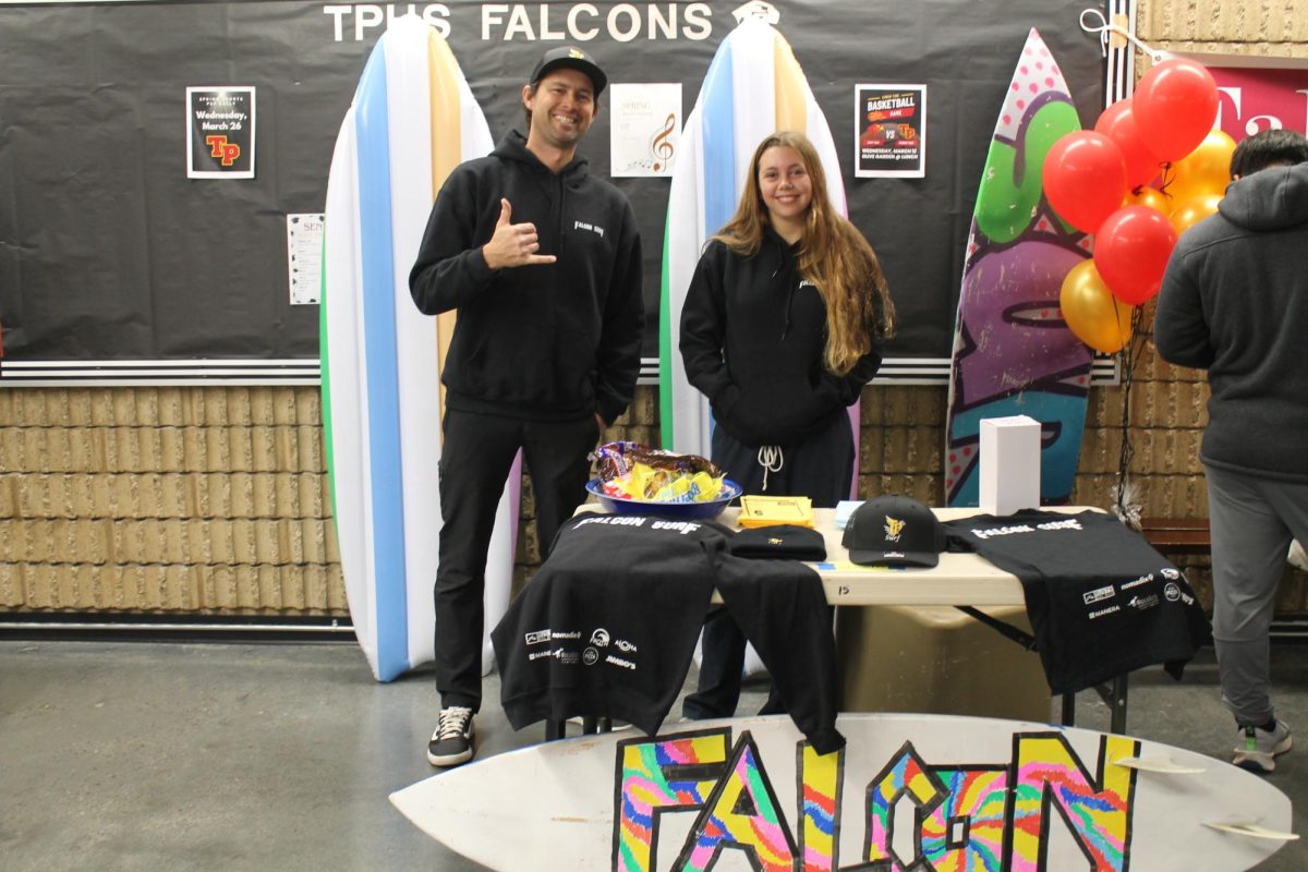 Surf PE teacher Austin Wade and Violet Evans (9) smile for a photo. The booth included colorful surfboards and merchandise.