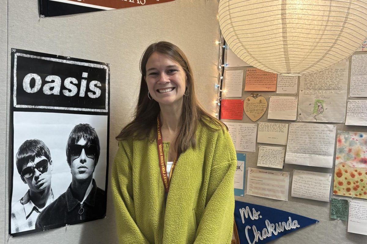 English 9 Honors and AP Language and Composition teacher Emily Chakurda stands in front of her favorite band Oasis' poster. Chakurda started teaching at TPHS this school year.
