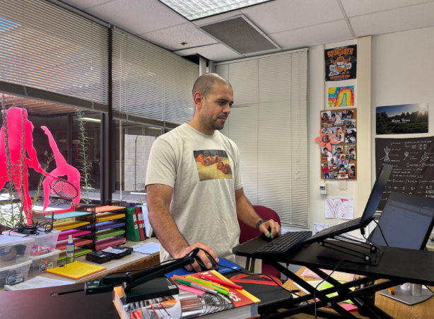 Integrated Math I teacher Noel Banuelos works at his computer, with colorful paper and craft supplies in the background. Banuelos began teaching in 2011 and joined the school’s math department this year. 
