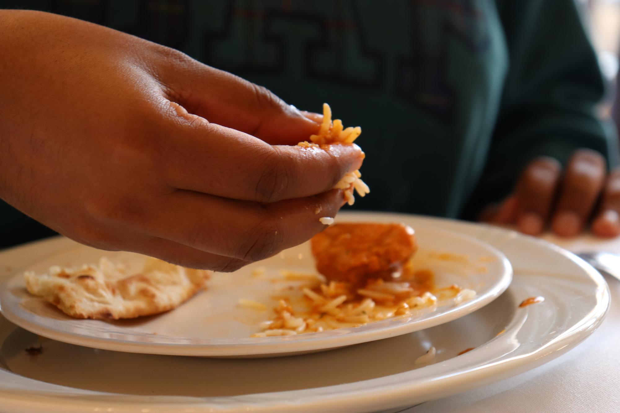 Iniya Sivakumar (11) scoops long-grain rice mixed with curry with her right hand, following Indian customs. She described eating with hands "like a language."