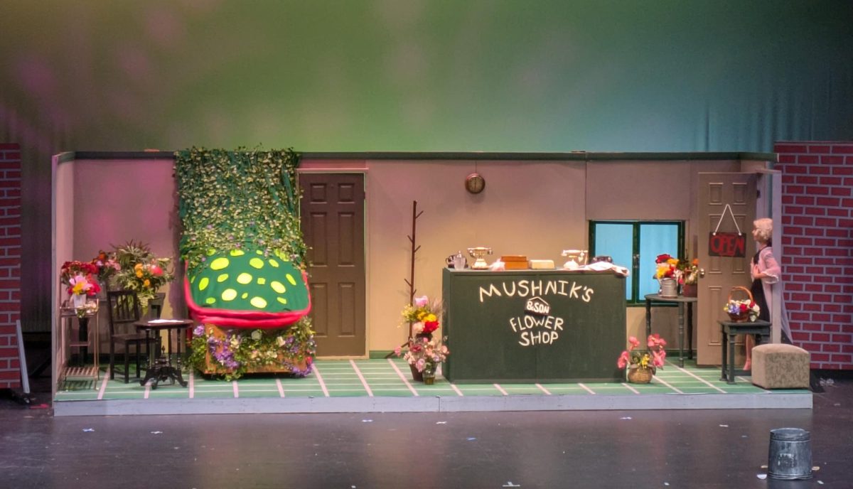 With neon green splotches and blood-red lips, the largest Audrey II puppet sits on the left side of the stage. Torrey Pines Players presented 'Little Shop of Horrors' from Feb 19  to 21 and Feb 26 to 28. Photo courtesy of Sandra Geminiani.