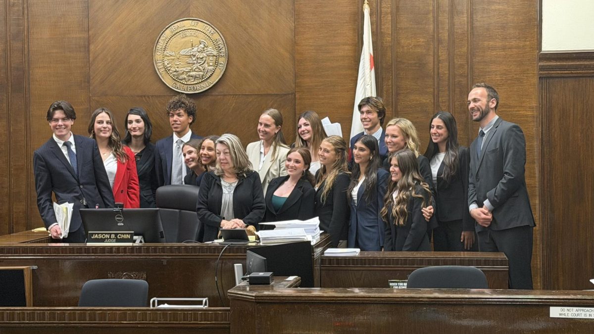 (Left to right) Braden Pegg (10), Caitlyn Van Hoose (12), Uma Zaric (11), Dean Smith (12), Lucinda Fleming (12), Maya Washington (11), Viktoria Kiss (11), Tess Franklin (10), Bianca Dwek (11), Sage Rosskopf (11), Cade Barber (12), Mira Panchal (10), Jennifer Nelson, Taylor Faaseen (12), Ella Kaplan (12) and John Milner pose at the René C. Davidson Courthouse. The team placed first out of 44 schools at the San Diego County competition. Photo courtesy of Dean Smith. 